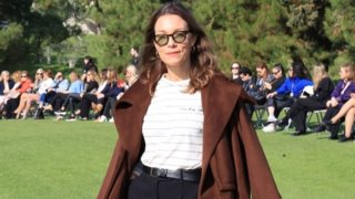 Η Βίκυ Καγιά με καφέ κάπα και bermuda shorts σε επίδειξη μόδας